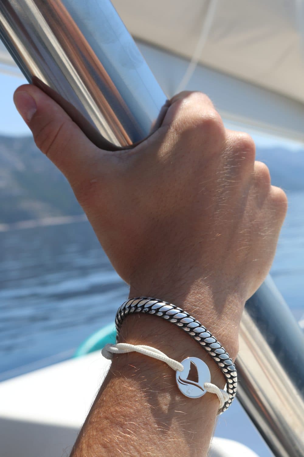 Gaab shark coin bracelet on a white cord, worn on a wrist on a boat at sea