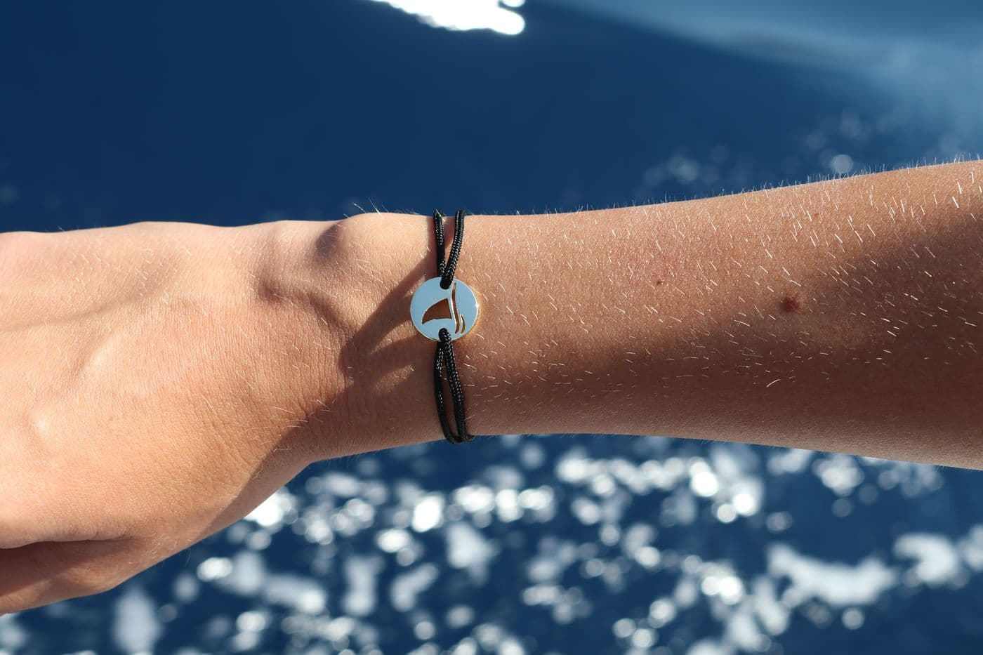 Gaab sailboat coin bracelet worn over sparkling blue water