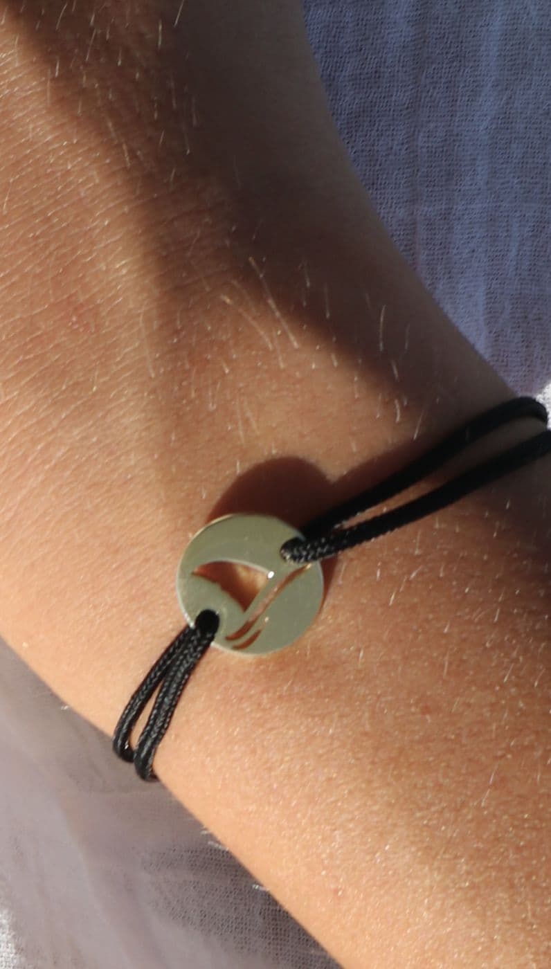 Close-up of a Gaab coin bracelet on black cord