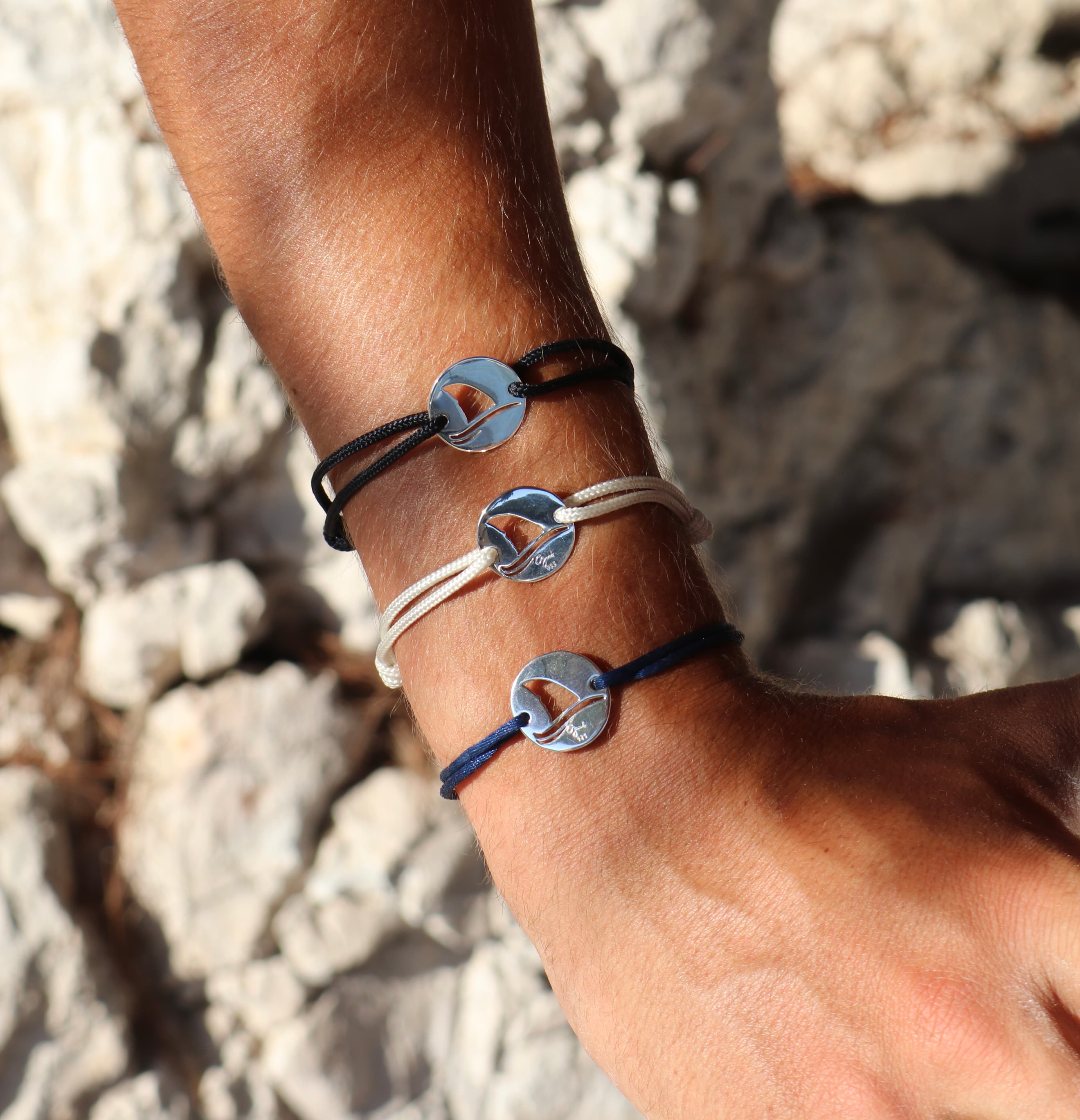 Three Gaab shark coin bracelets stacked on a wrist above white rocks